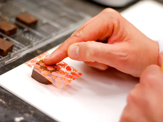 In this image we can see a person's hand placing a creative cover on the chocolate. On the left...