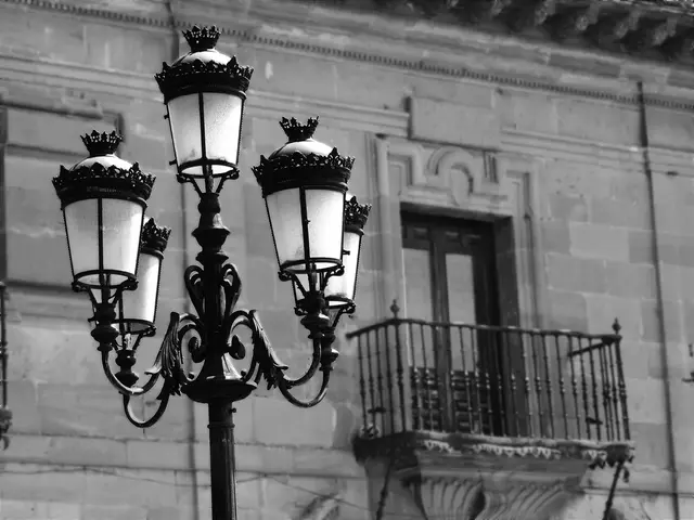 This is a black and white image. On the left side there is a pole which consists of five lanterns....